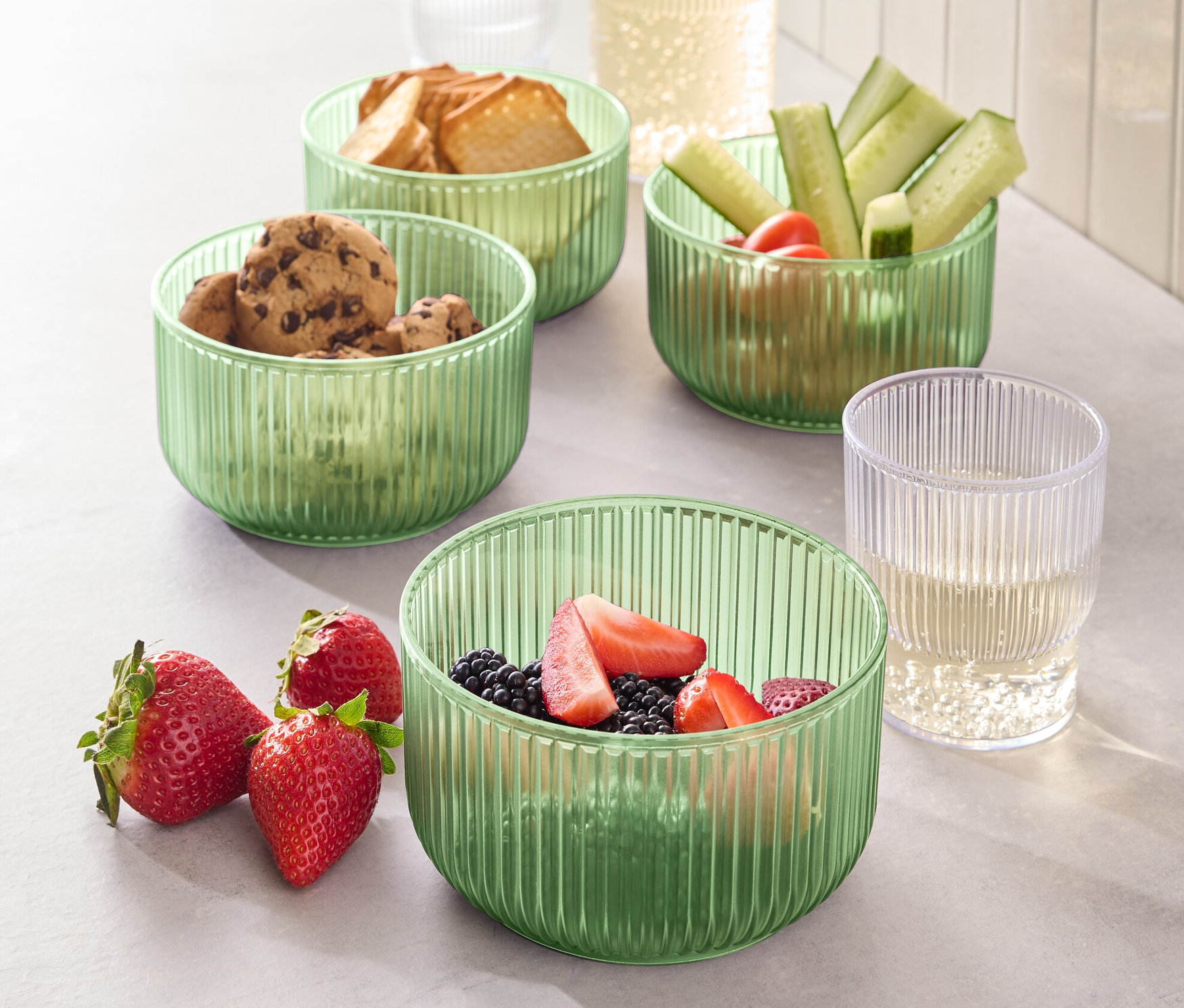 Négy műanyag tál étellel, köztük süteményekkel, kenyérrel, uborkával és eperrel.