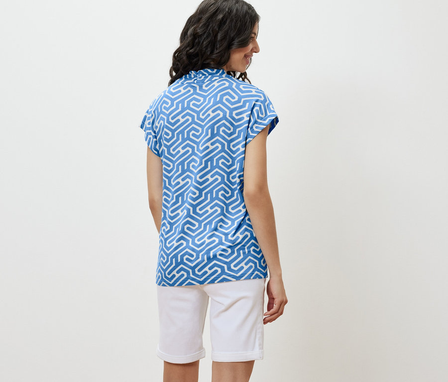 Nő visel kék, V-nyakkivágású pólóblúzt és fehér rövidnadrágot.