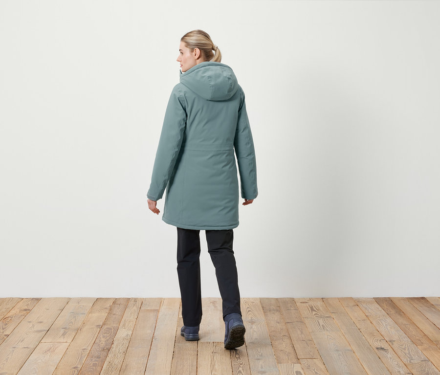 Egy nő háttal a kamerának kapucnis kabátot és sötét nadrágot visel.