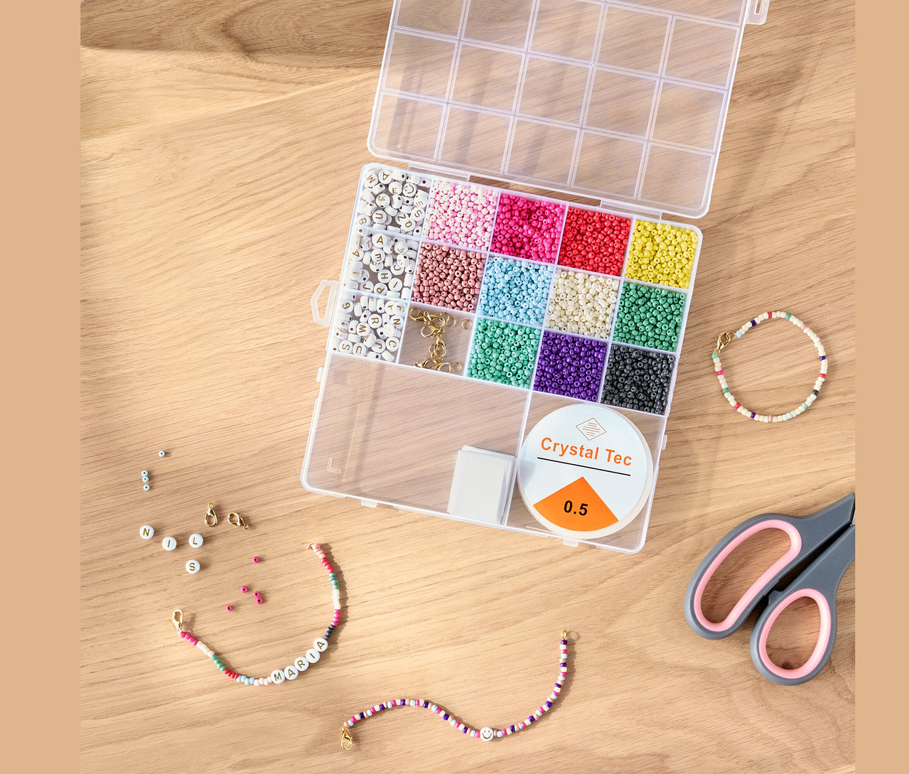 Nyitott DIY gyöngykészlet színes gyöngyökkel, zsinórral és ollóval egy fa asztalon.