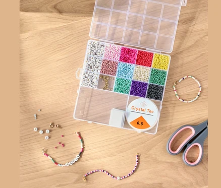Nyitott DIY gyöngykészlet színes gyöngyökkel, zsinórral és ollóval egy fa asztalon.
