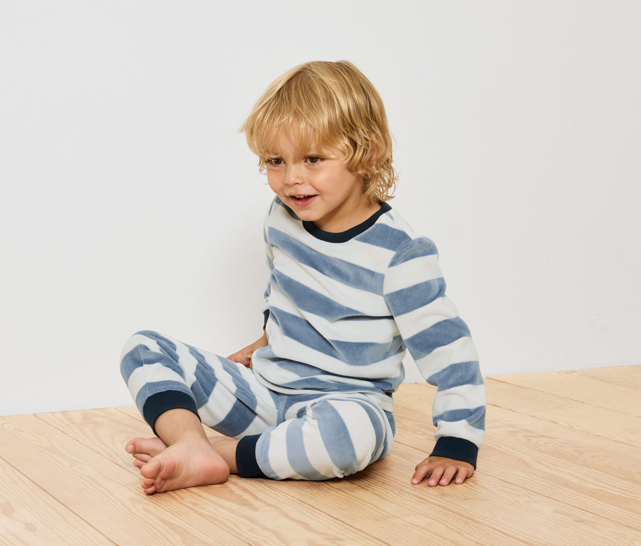 Fiú ül csíkos pizsamában a fapadlón.