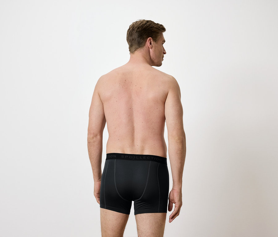 Egy férfi hátulnézete fekete boxeralsóban, fehér háttér előtt.