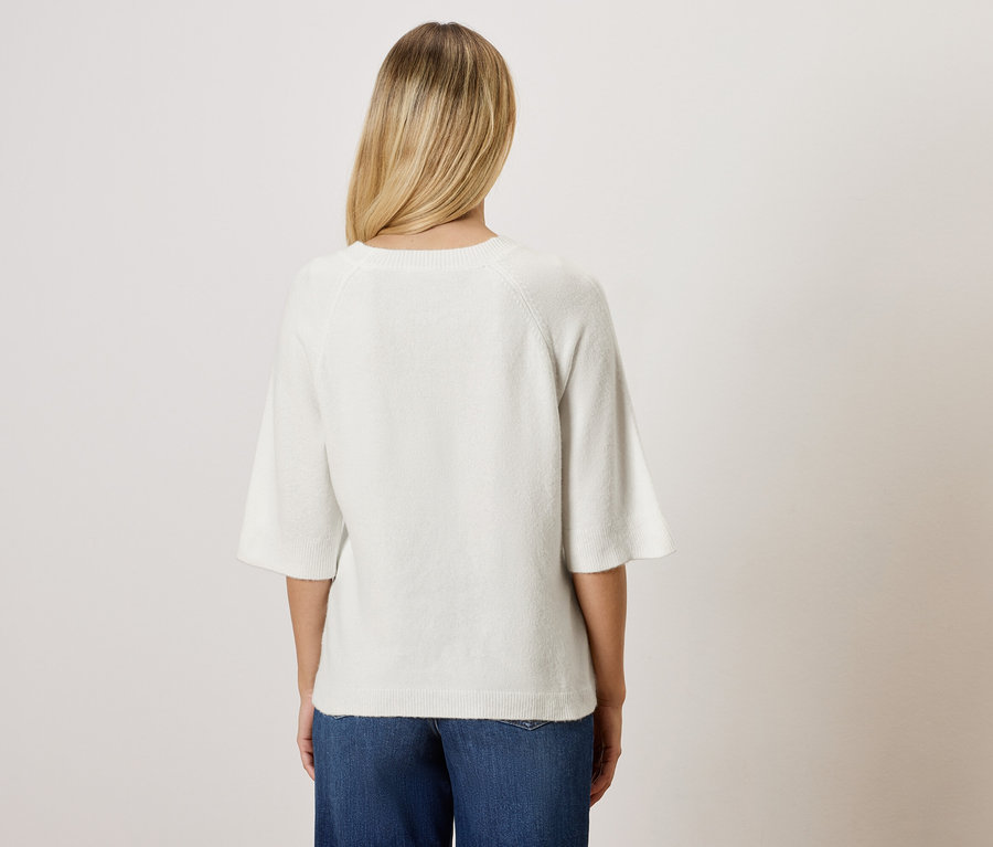 Hátulnézet egy szőke hajú nőről fehér blúzban és kék farmerban.