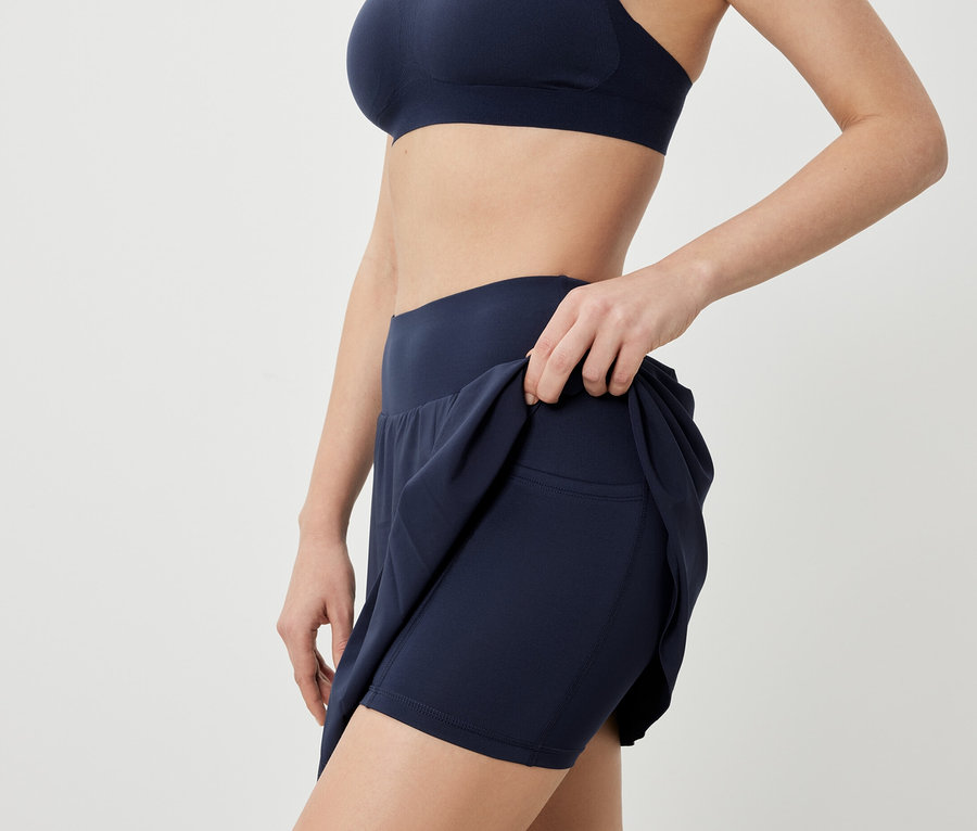 Nő sportmelltartót és sötétkék sportszoknyát visel.