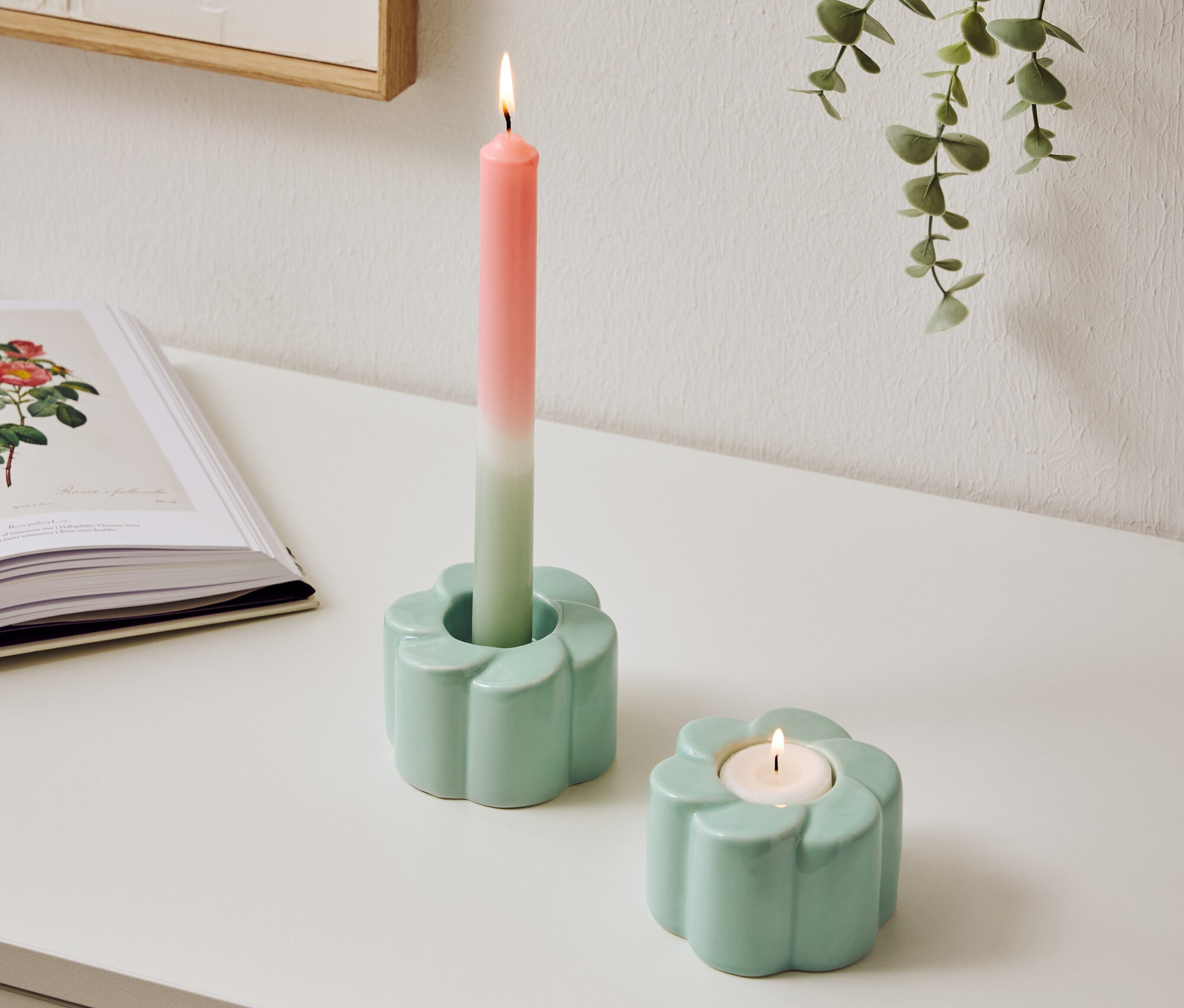 Két világoskék, virág alakú gyertyatartó áll az asztalon, az egyikben égő, kétszínű gyertya van.