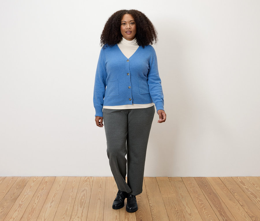 Nő krémfehér garbónyakú felsőben, kék kardigánban és szürke nadrágban.