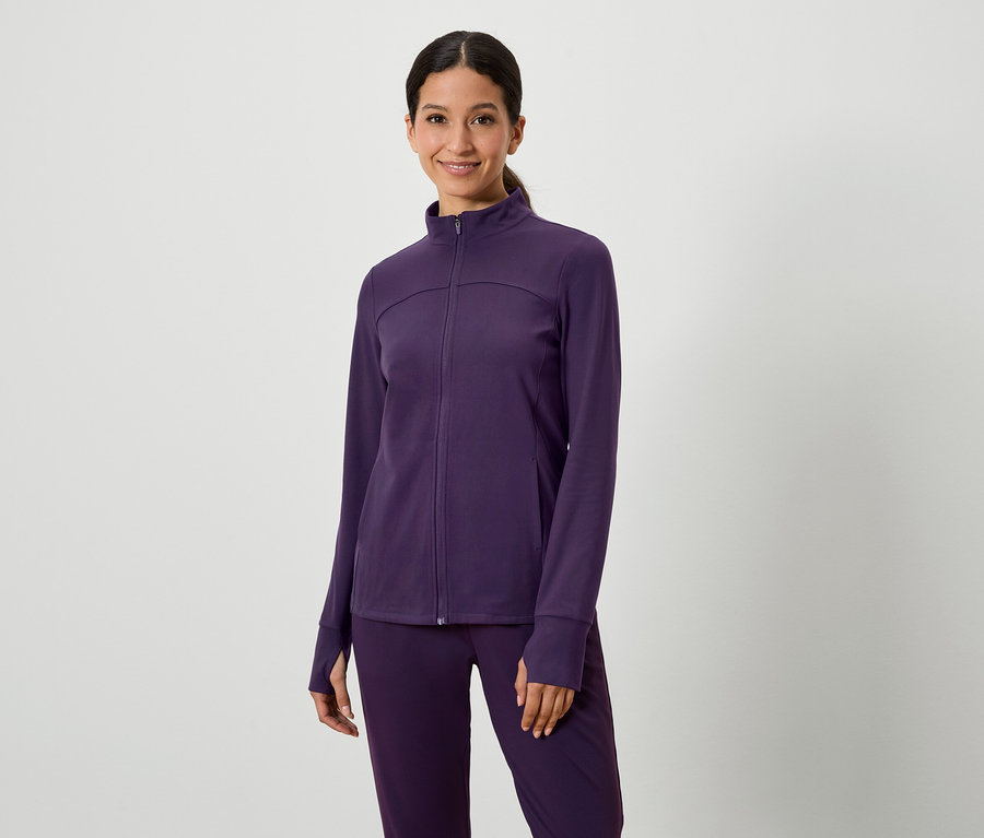 Nő pózol lila kabátban és nadrágban.