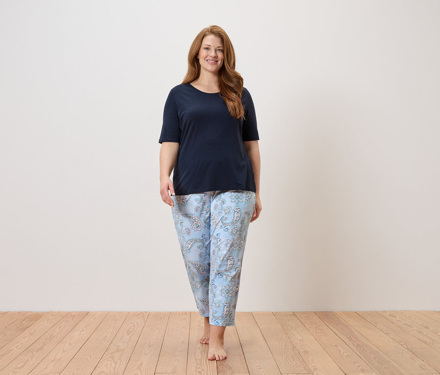 Nő mezítláb sétál tengerészkék felsőben és világoskék, paisley mintás nadrágban.