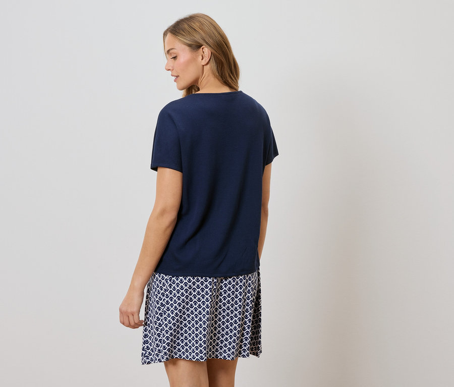 Hátulnézet egy szőke hajú nőről, aki sötétkék pólót és kék-fehér mintás szoknyát visel.