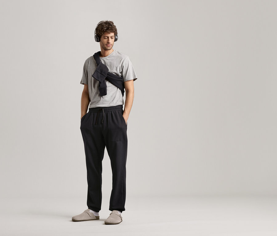 Férfi fejhallgatóval, szürke pólóval és fekete szabadidőnadrággal, semleges háttér előtt.