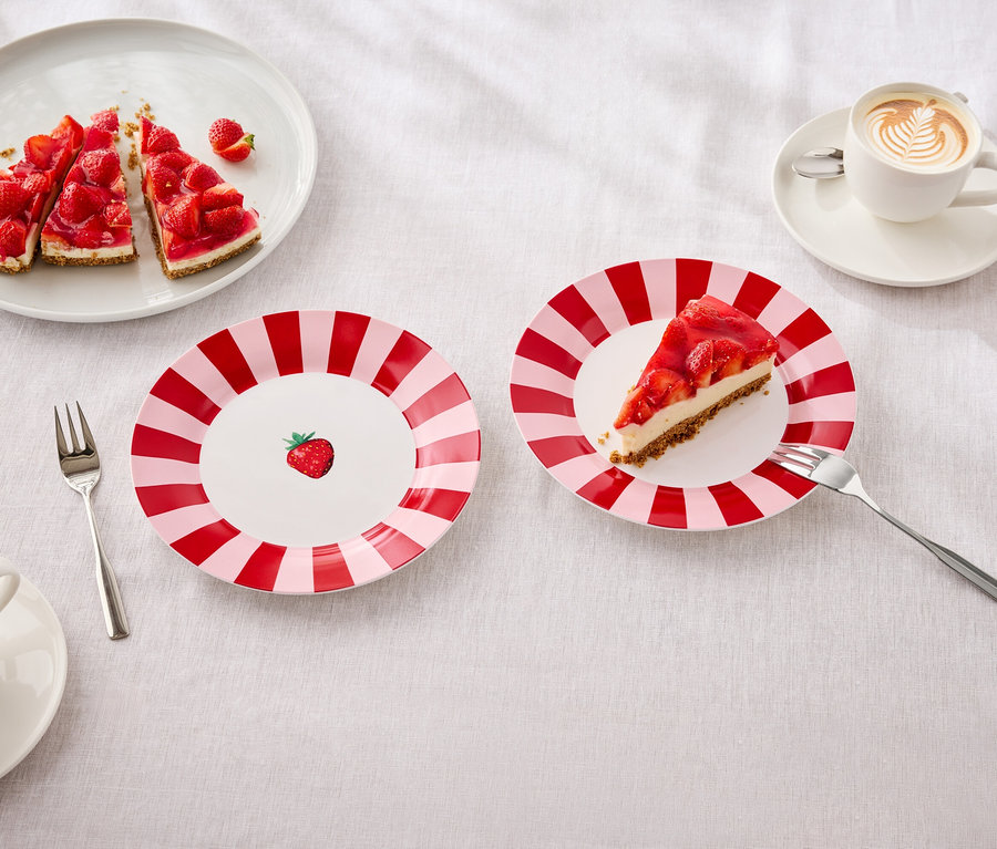 Az asztalon tányérok epertortával, villák és latte artos csészék találhatók.