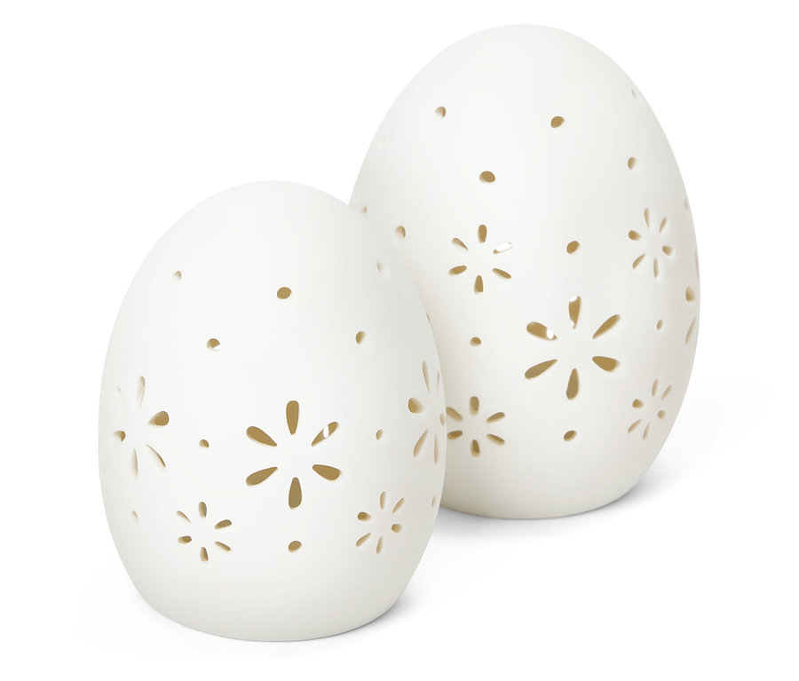 Két fehér dekorációs tojás kivágott virágmintákkal fehér háttér előtt áll.