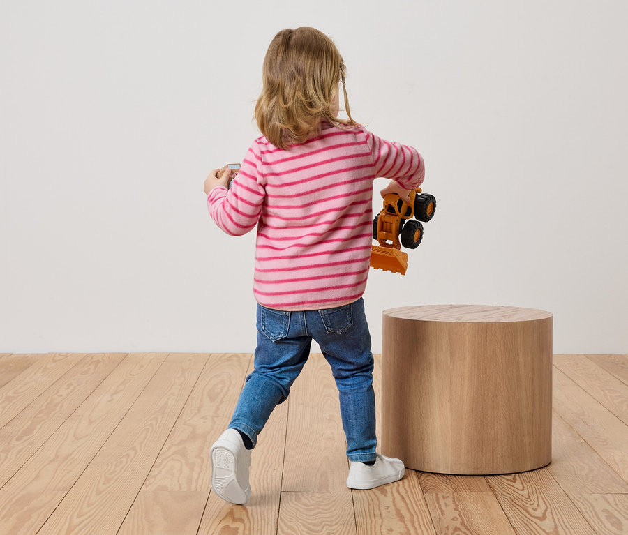 Egy szőke hajú gyermek háttal áll a nézőnek, és egy játék markolót tart a kezében.