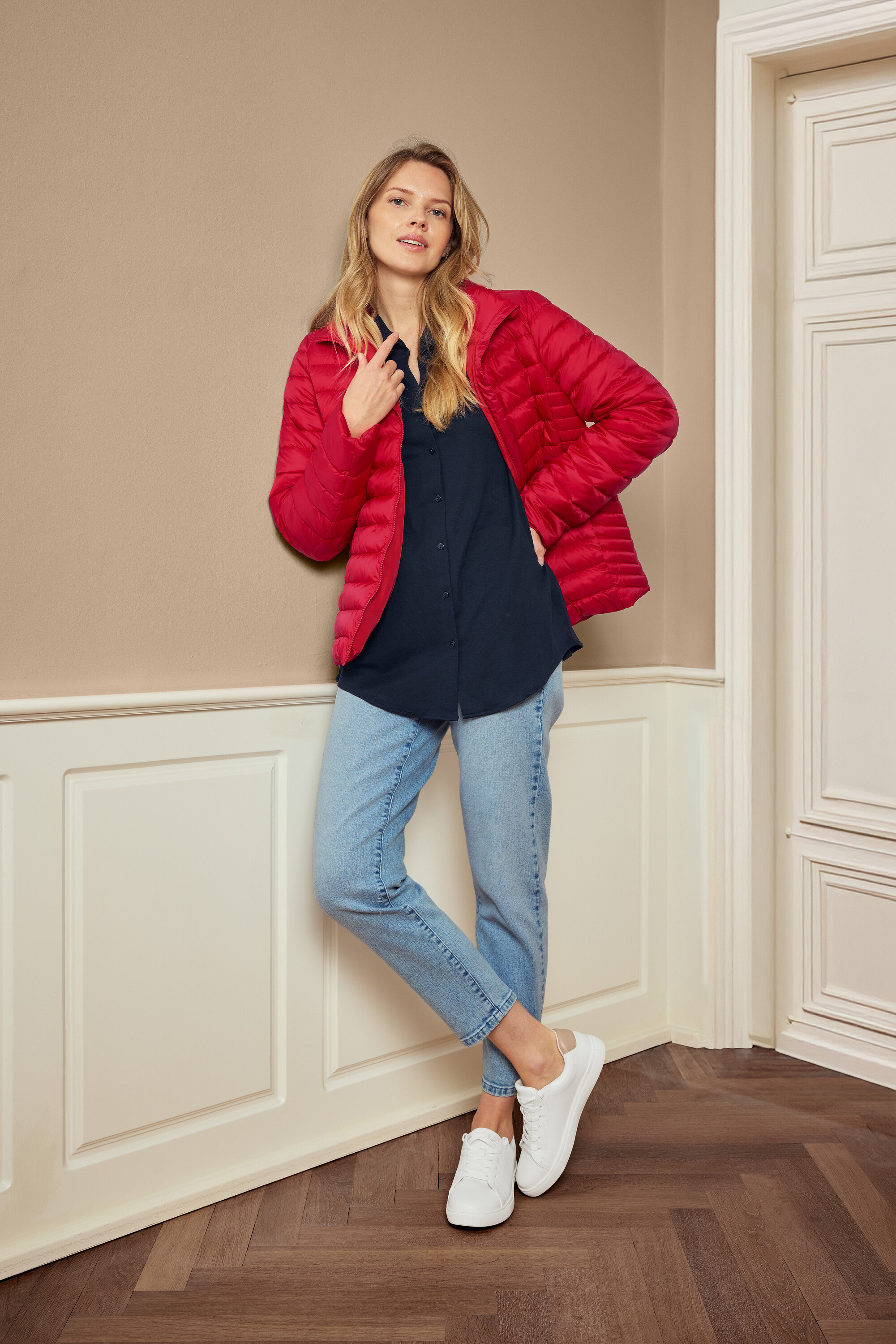 Nő pózol piros kabátban, kék ingben, farmerban és fehér tornacipőben, 925 Silber Creolen Hexagon fülbevalót visel.