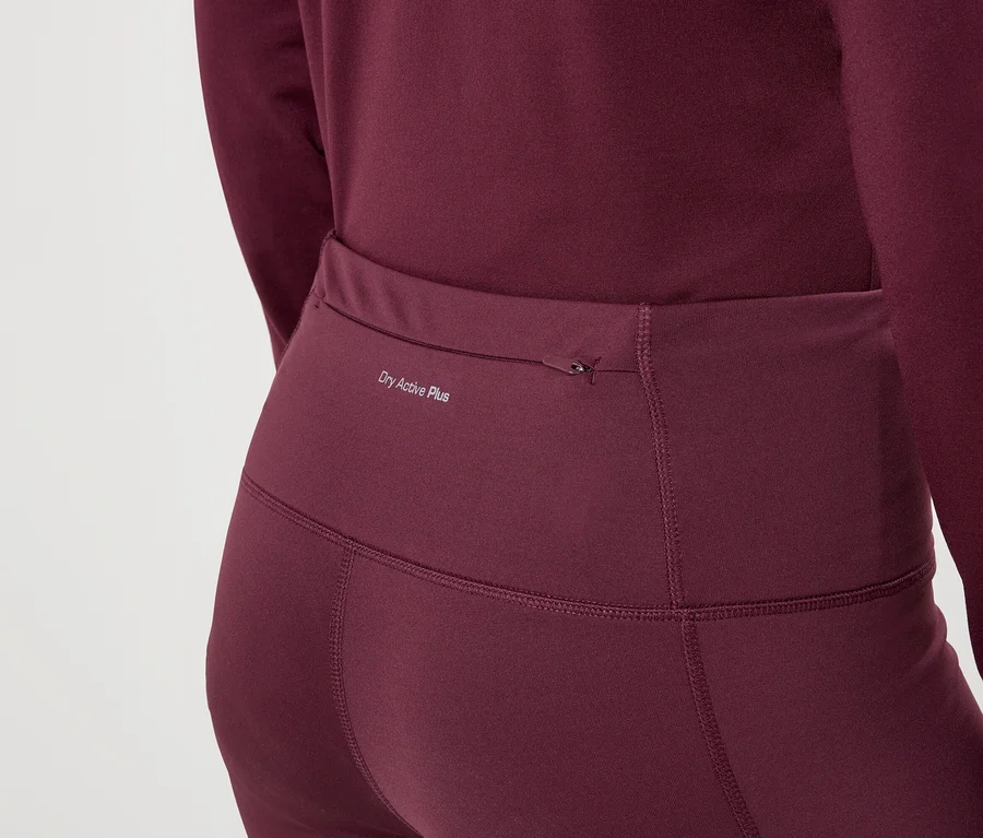 Egy nő közeli képe bordó színű leggingsben és hosszú ujjú felsőben, rajta a „Dry Active Plus” felirat.