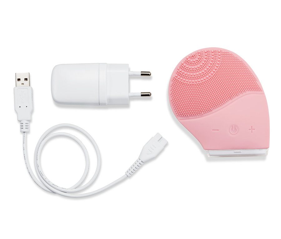 Egy rózsaszín elektromos szilikon arctisztító kefe töltőkábellel és adapterrel.