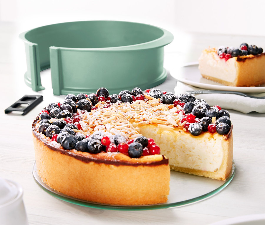 Sajttorta áfonyával és ribizlivel, szeletelve egy tányéron, egy szilikon sütőforma üvegaljjal mellett.