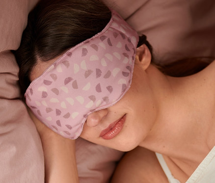 Nő alszik egy súlyozott alvómaszkban az ágyban.