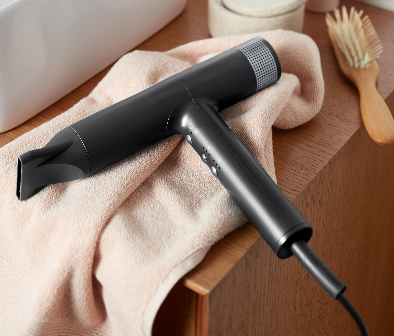 Egy fekete prémium hajszárító új szárítási technológiával egy rózsaszín törölközőn fekszik egy mosdókagyló mellett.