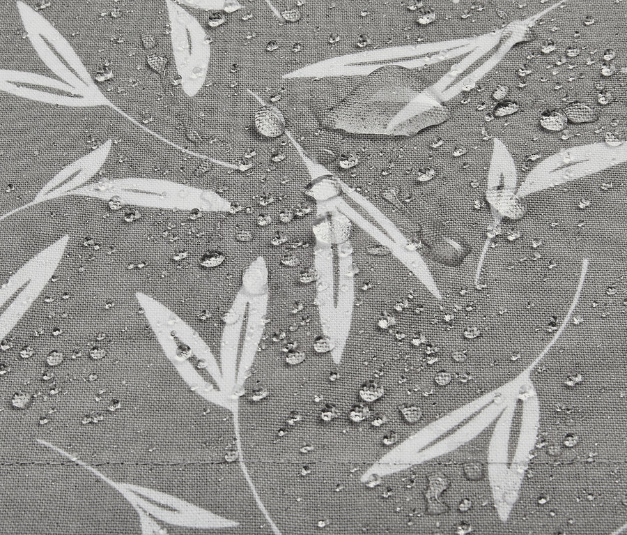 Egy szürke kültéri asztalterítő részlete fehér levélmintával és vízcseppekkel.