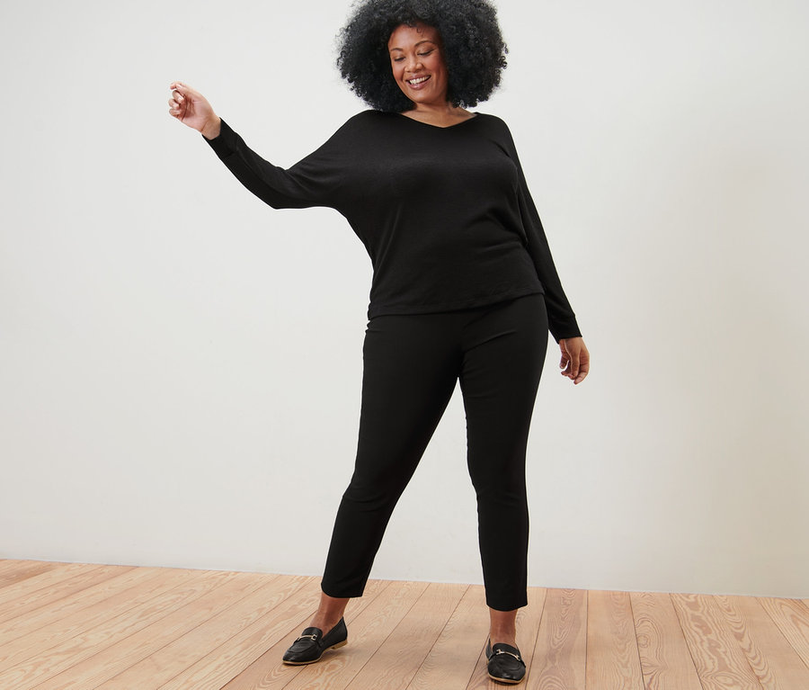 Nő pózol fekete denevérujjú felsőben és fekete sztreccsnadrágban.