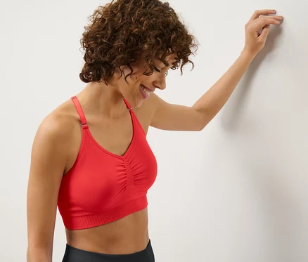 A falnak dőlő nő piros, női bustier sportmelltartót visel.