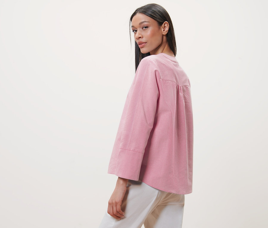 Nő néz a válla fölött, rózsaszín-fehér csíkos blúzt visel.