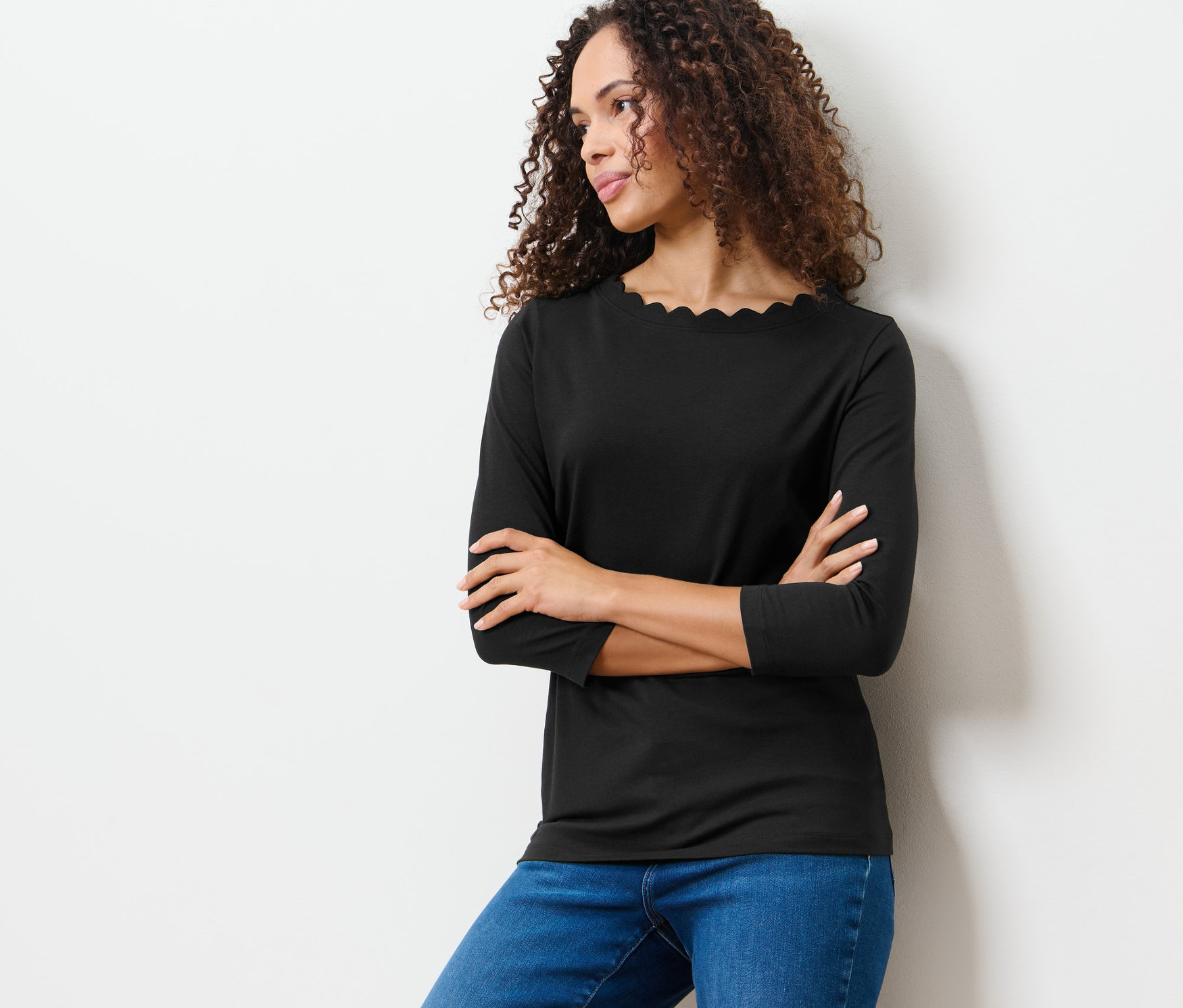 Nő pózol egy fekete, 3/4-es ujjú felsőben.