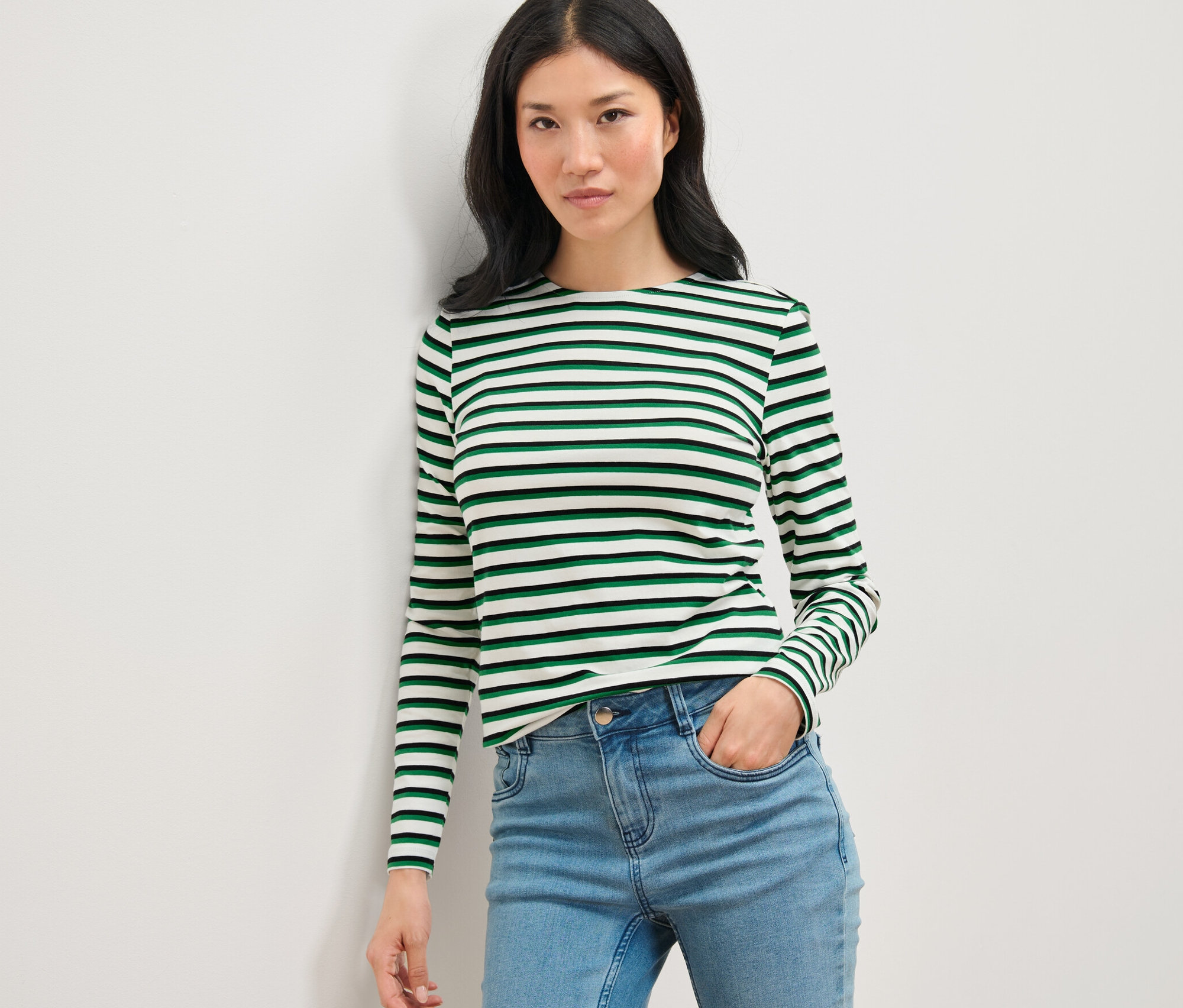 Nő pózol egy csíkos, hosszú ujjú felsőben és farmerban.
