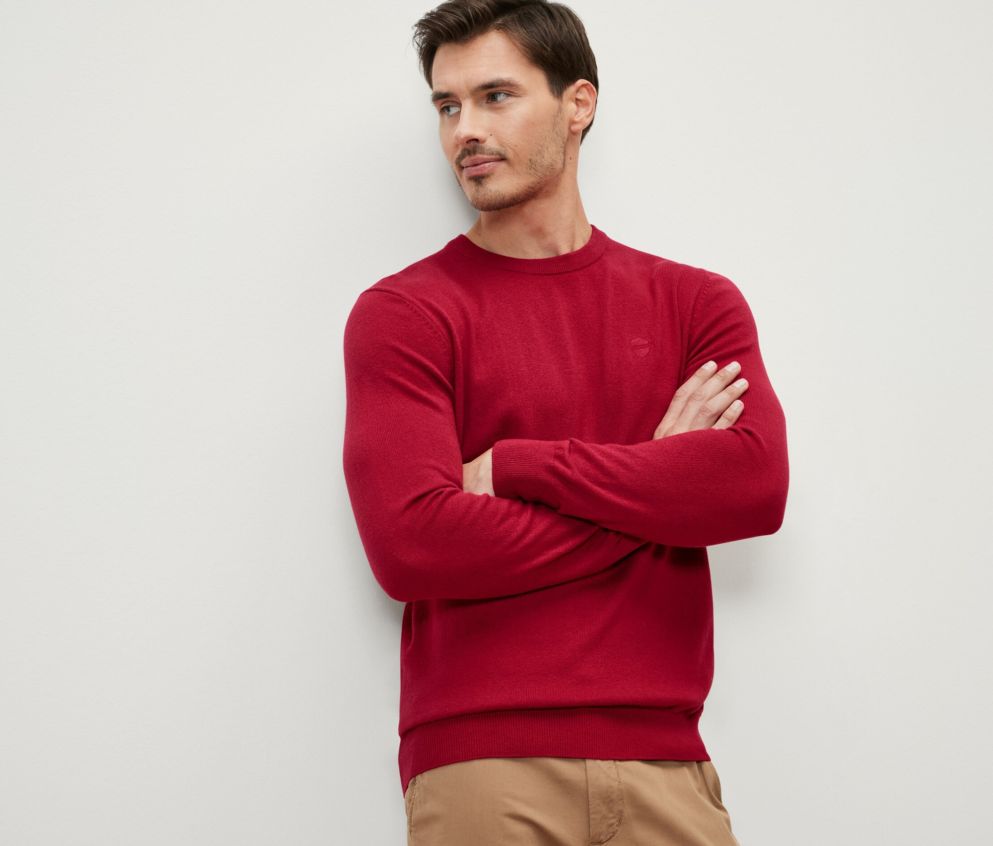Férfi keresztbe tett karokkal piros kötött pulóvert visel.