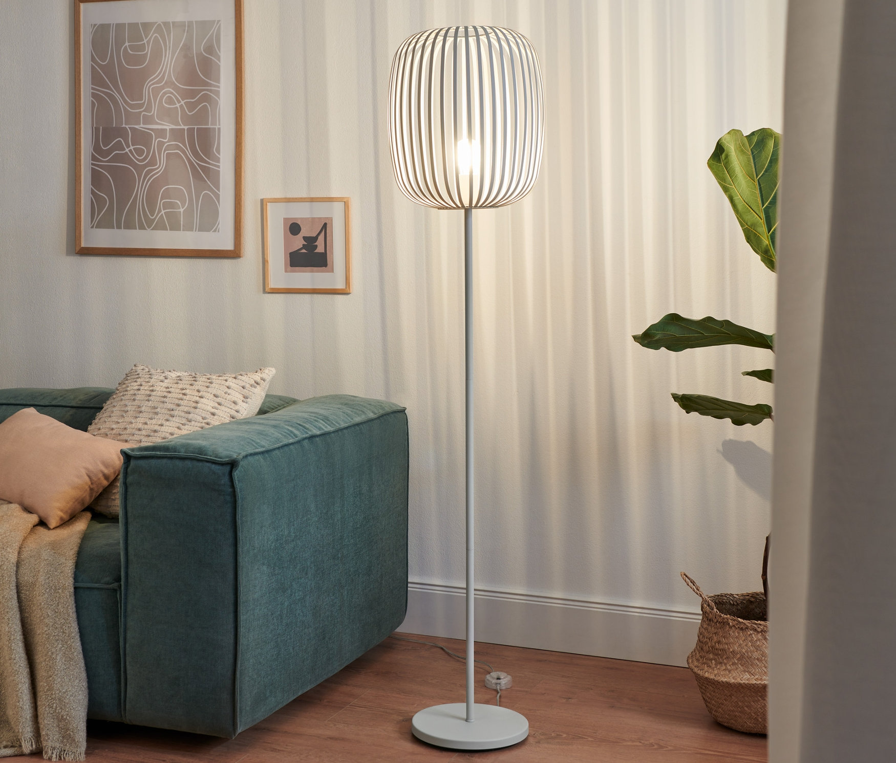 Egy fém állólámpa áll egy zöld kanapé mellett egy nappaliban.