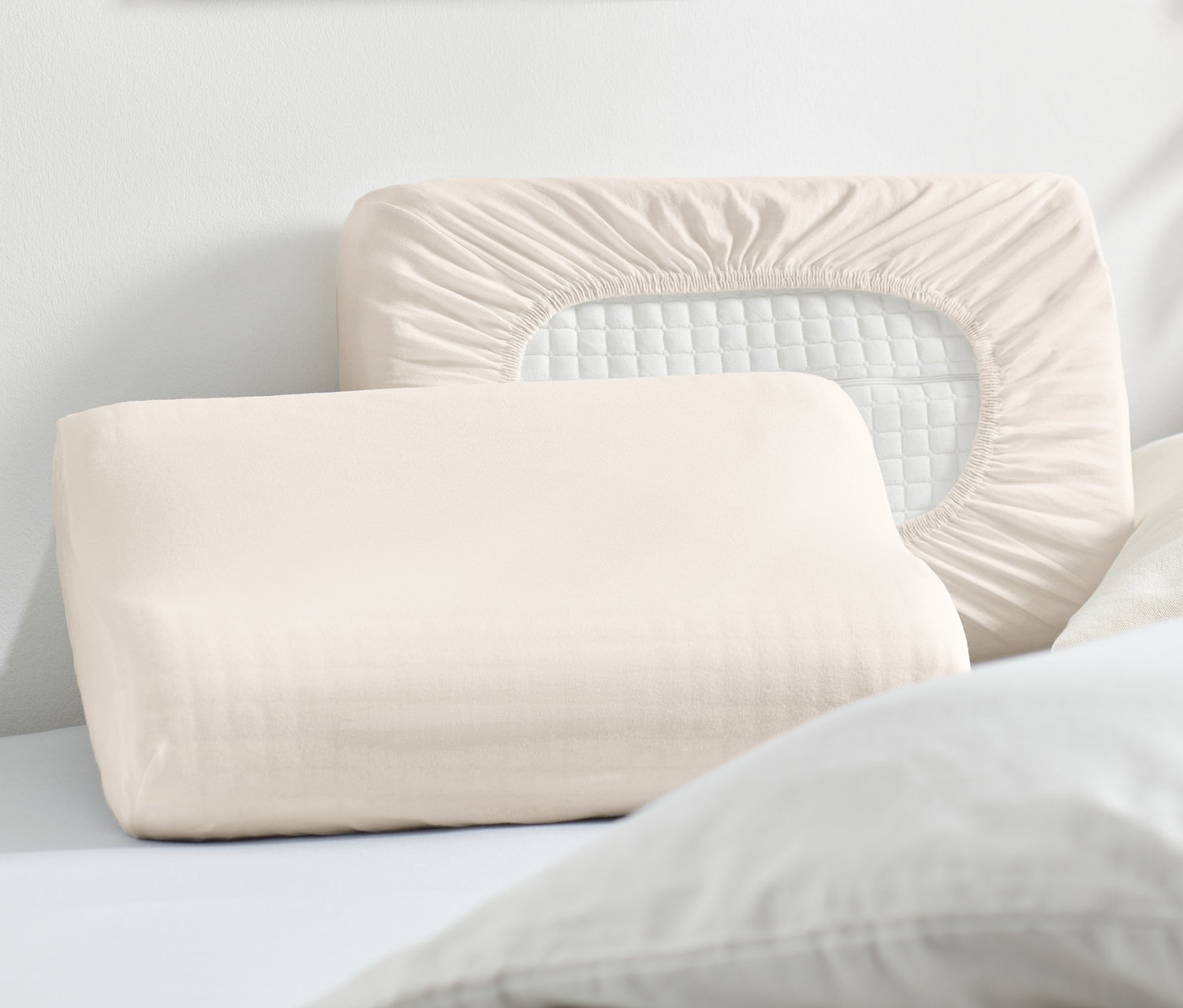 Két bézs színű jersey gumis párnahuzat fekszik egy ágyon.