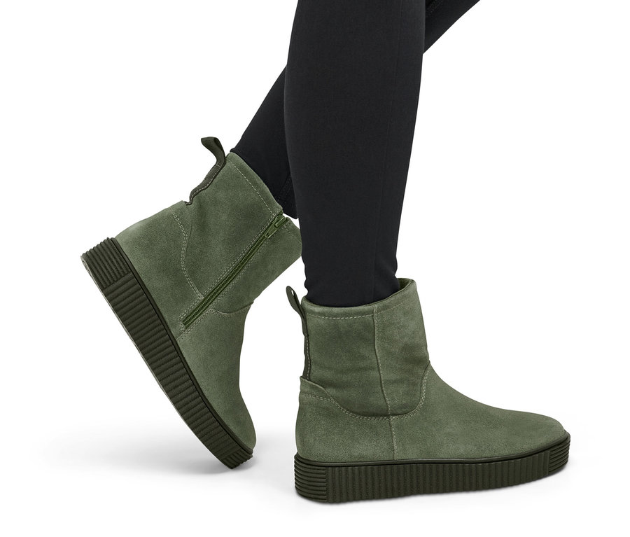 Fekete leggingset és zöld női velúrbőr csizmát viselő lábak.