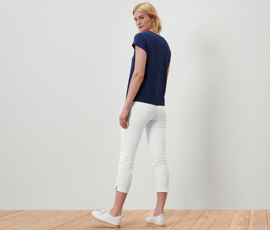 Egy nő háttal áll a kamerának, fehér 7/8-os sztreccsnadrágot és sötétkék pólót visel.