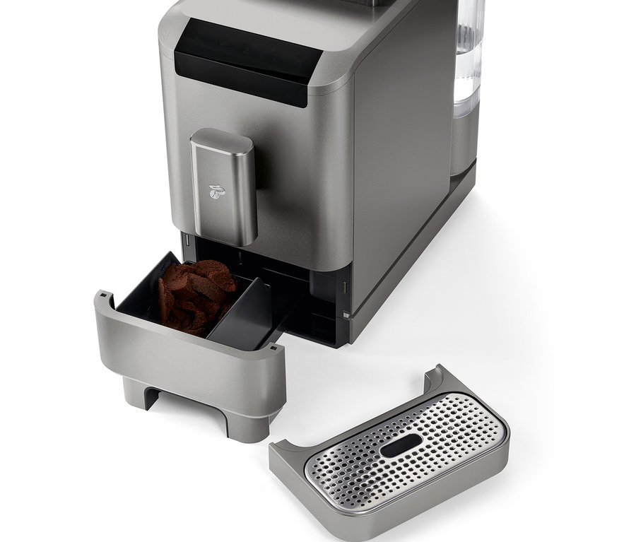 Közelkép a »Esperto2 Caffè« automata kávéfőzőről Titanium Silver színben, eltávolított kávézacc-tartállyal és csepptálcával.