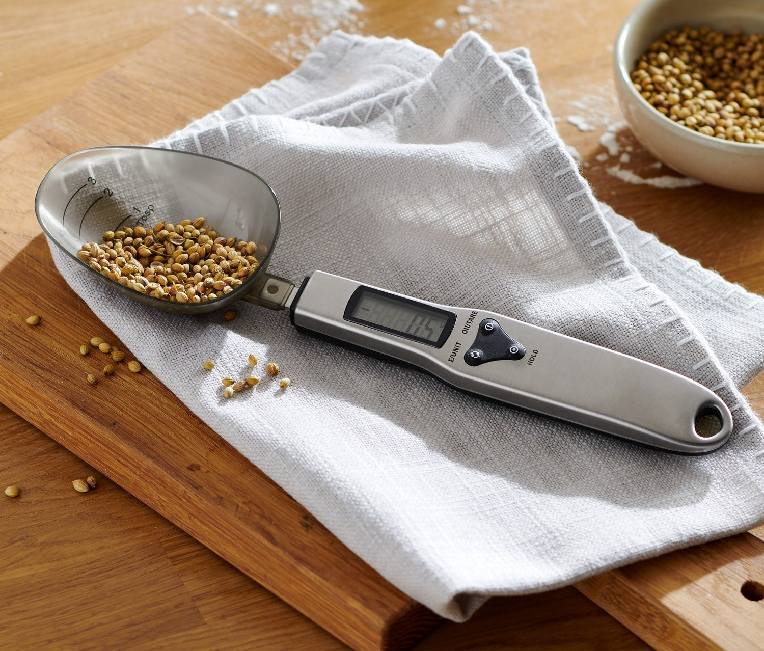 Digitális kanálmérleg fűszerekkel egy deszkán tésztás tál mellett.