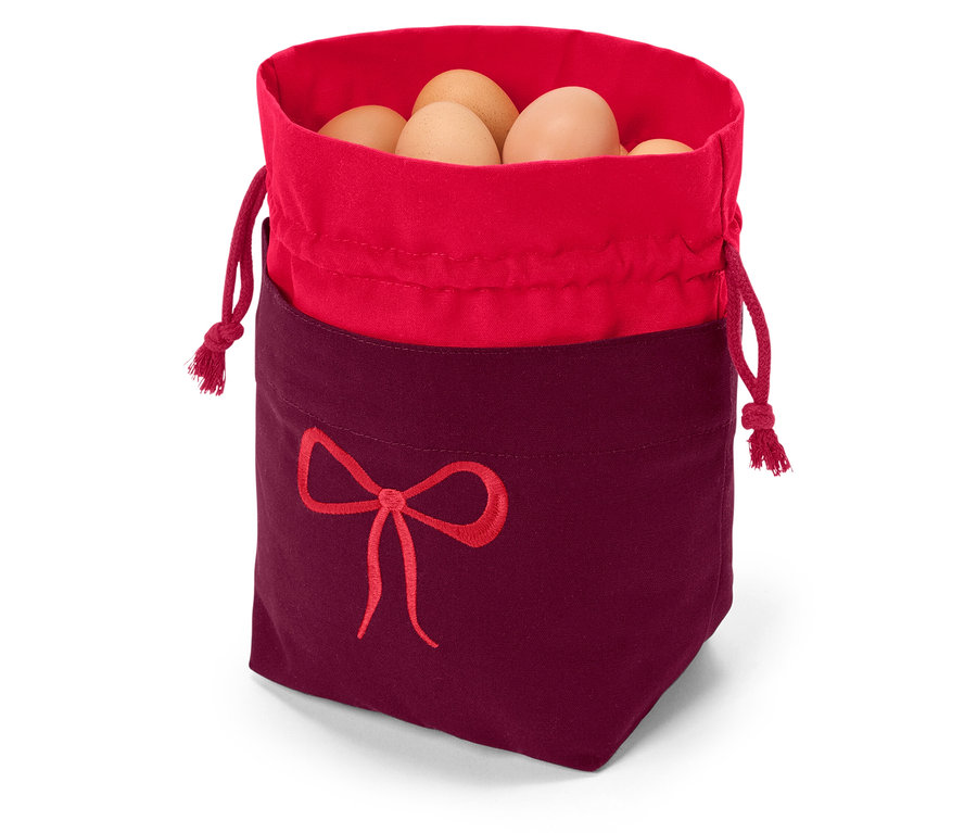 Piros szegélyű és bordó aljú szövetzsák, piros masni hímzéssel díszítve, barna tojásokkal tele.