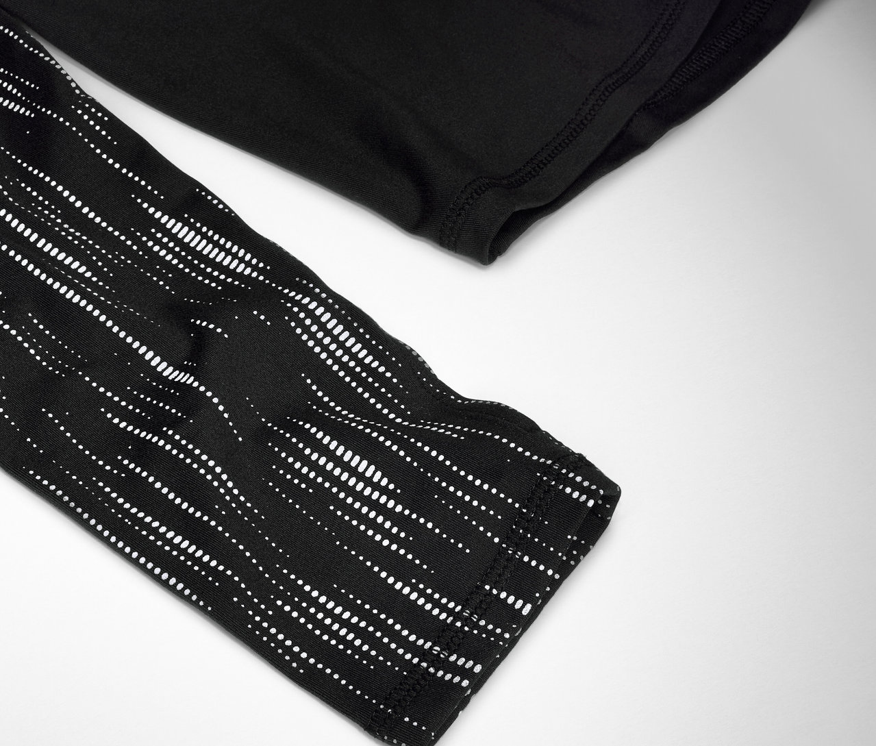 Egy fekete, hosszú ujjú póló részlete, fehér pöttyös mintával az ujján.