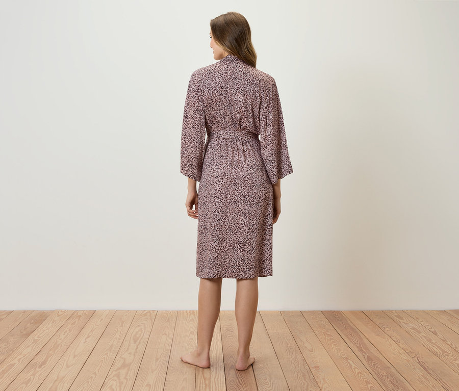 Egy nő háttal áll a kamerának, és rózsaszín, mintás köntöst visel.