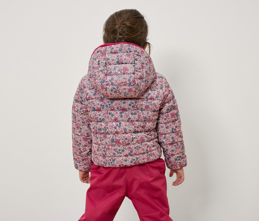 Egy kislány háttal a kamerának virágos kabátot és rózsaszín nadrágot visel.