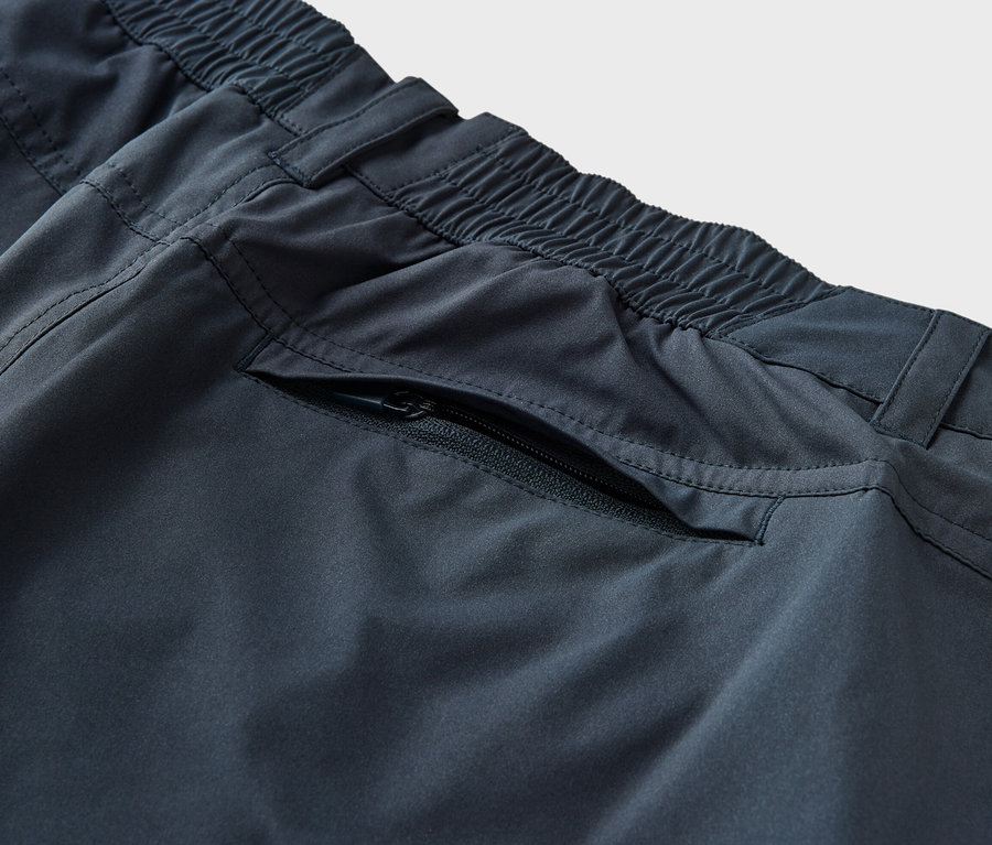 Egy sötétkék, 2 az 1-ben funkcionális nadrág részlete, gumis derékkel és cipzáras zsebbel.