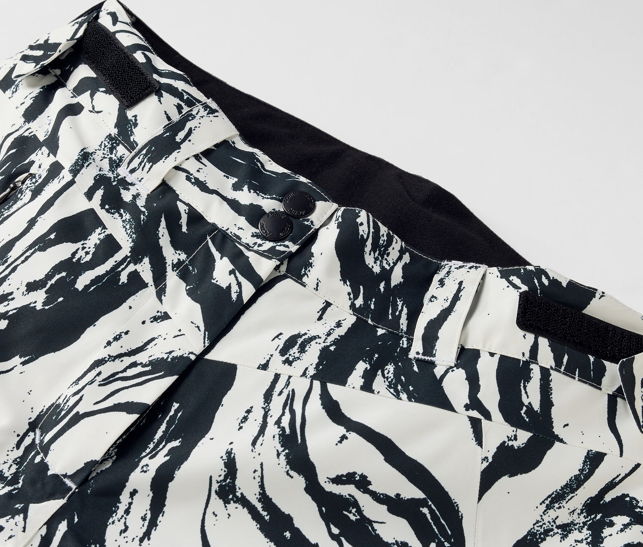 Egy fekete-fehér mintás nadrág részlete, gombos zárással és fekete derékpánttal.