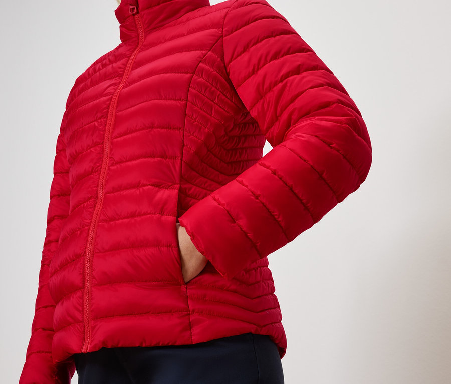 Egy személy a kezét egy piros steppelt kabát zsebében tartja.