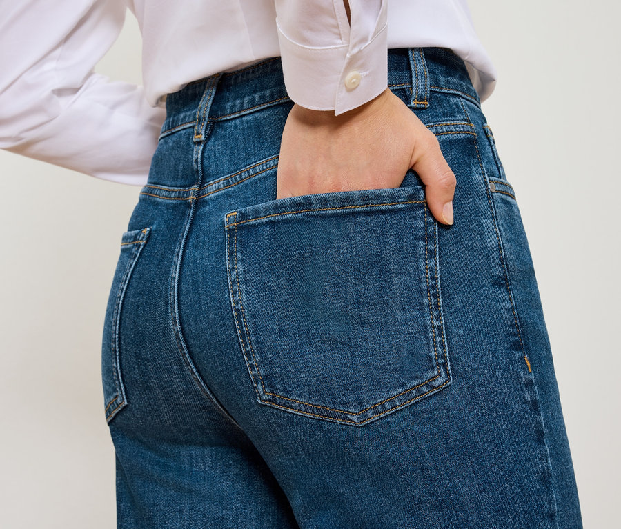 Hátulnézet egy nőről, akinek a keze a kék Mom Jeans – Fit »Nyla« zsebében van.