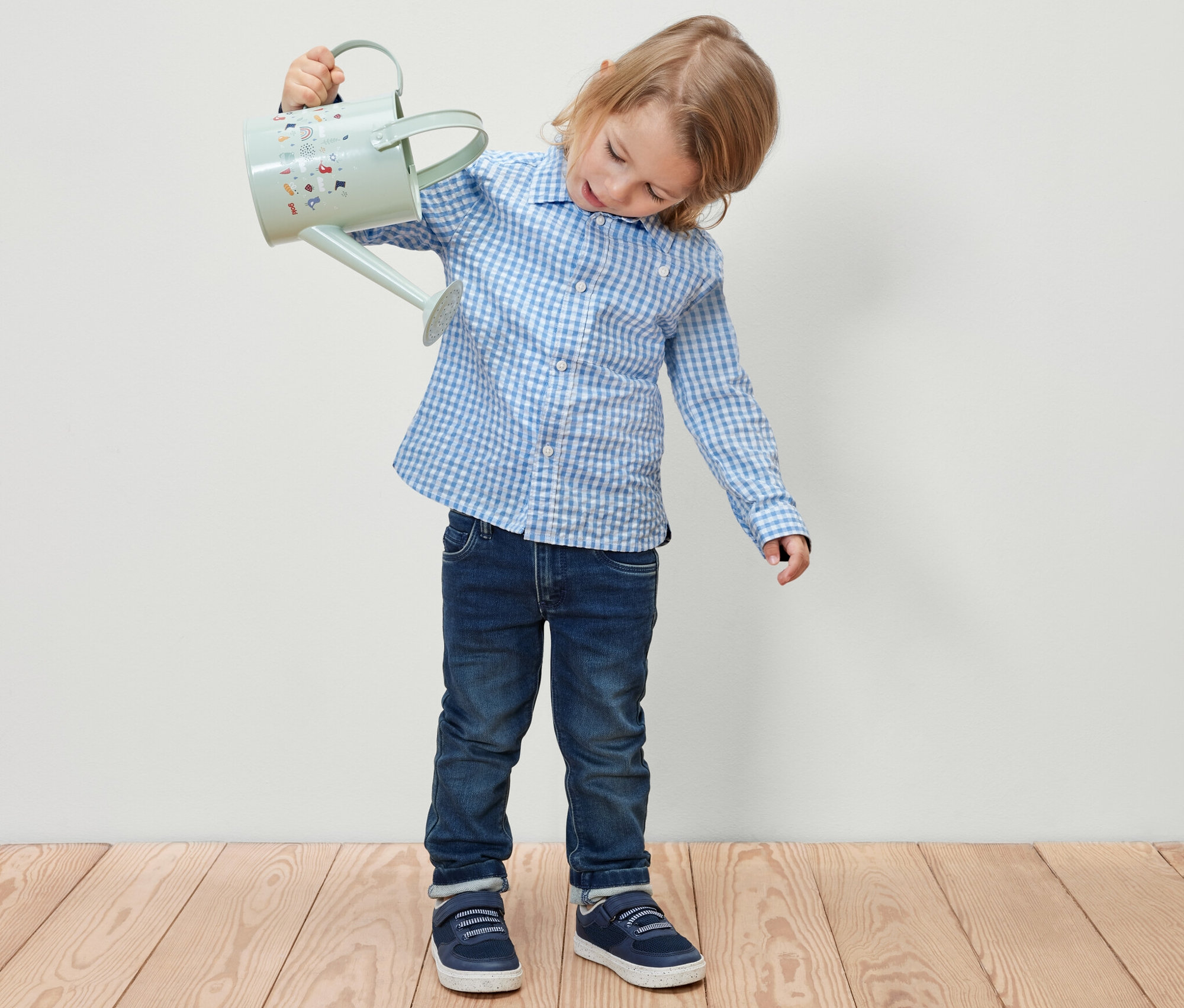 Fiú világoskék locsolókannát tart a kezében. Kisfiú ing van rajta.