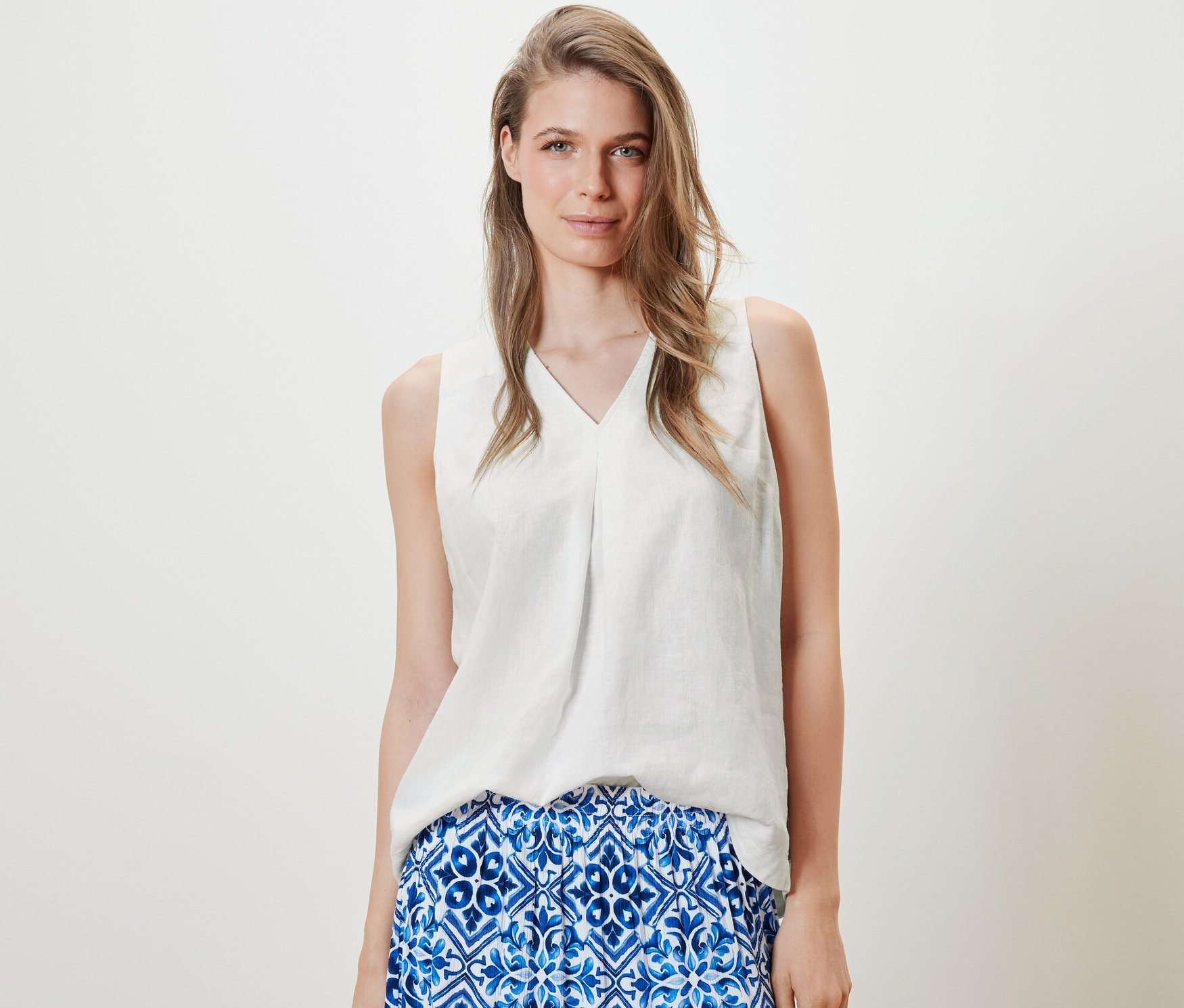 Nő visel fehér, ujjatlan lenvászon blúzt és kék szoknyát.