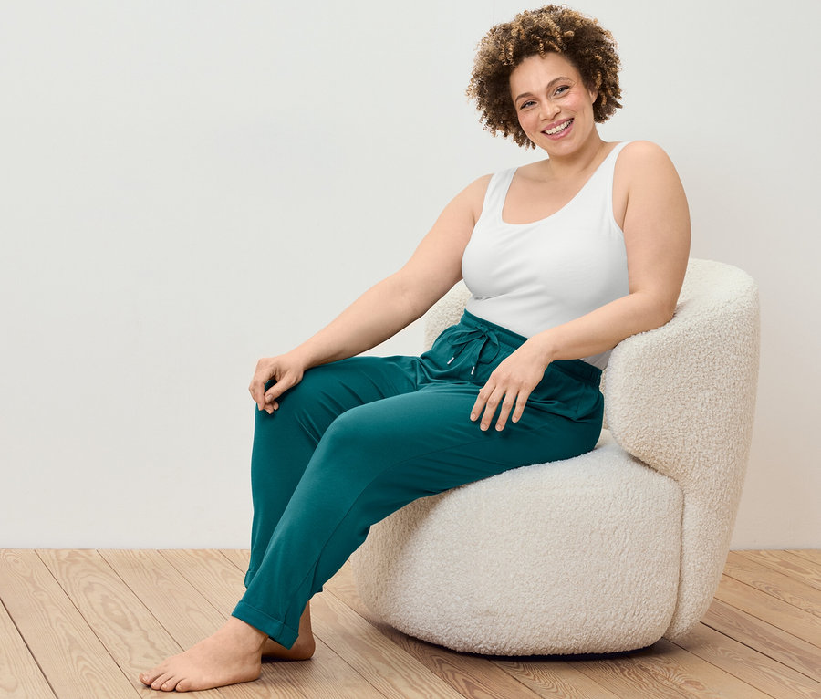 Nő ül a székben, 2 trikót és pizsamanadrágot visel.