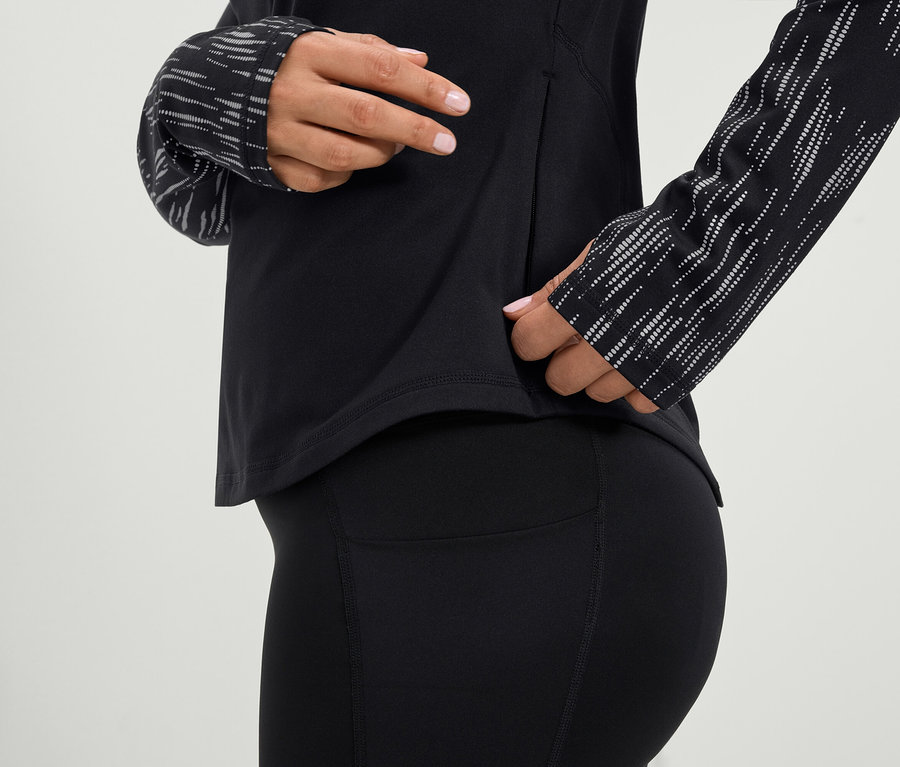 Nő nyúl egy fekete, hosszú ujjú sportfelső és egy fekete leggings oldalzsebébe.