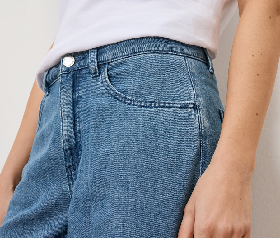 Közeli kép egy világoskék farmerban és fehér pólóban lévő nőről.